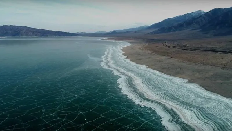 Зимний пейзаж Орто-Токойского водохранилища в Кыргызстане с замерзшей поверхностью озера и заснеженными горами