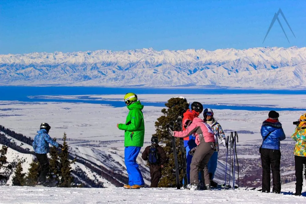 Tourists at one of the peaks of the Karakol ski base with a view of Issyk-Kul Lake